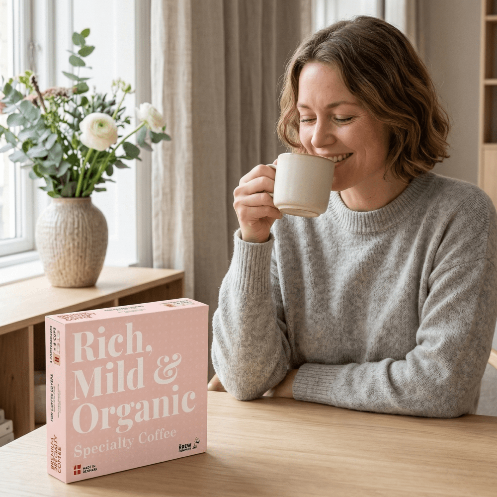 Woman drinking coffee next to a 'Rich, Mild & Organic' coffee box in a cozy room.