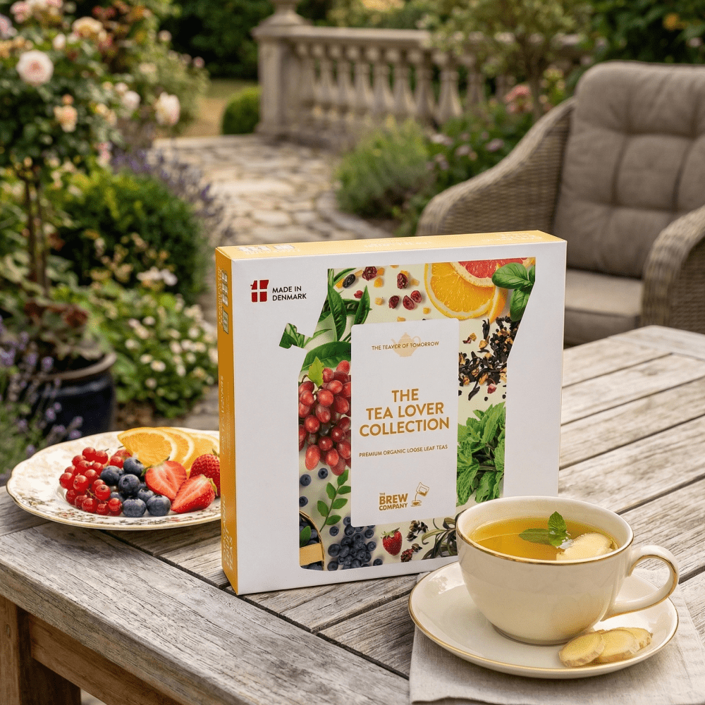 Tea box labeled 'The Tea Lover Collection' on a wooden table with a cup of tea and fruit plate outdoors.